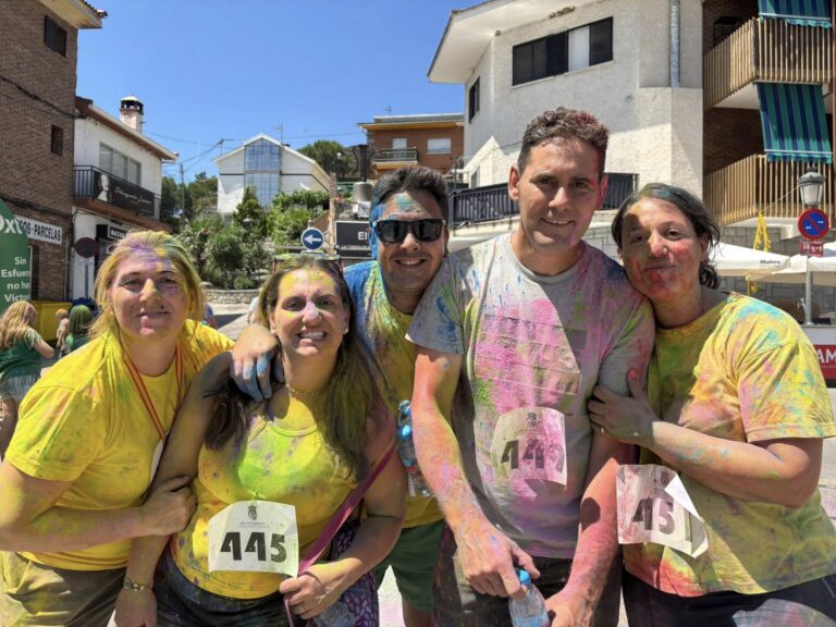 Cinco personas sonrientes, con camisetas y rostros cubiertos de polvo de colores, posando en lo que parece ser una carrera o actividad festiva, en El Boalo, Cerceda y Mataelpino.