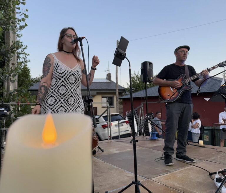 Músicos actuando en un escenario al aire libre durante la Noche en Vela, con una gran vela LED en primer plano, simbolizando el ambiente mágico que el Ayuntamiento crea en Mataelpino.