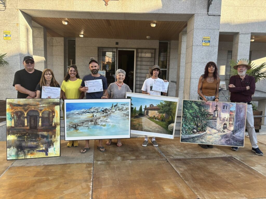 Un grupo de ocho artistas, algunos sosteniendo pinturas y diplomas, posan sonrientes frente a un edificio moderno tras el Concurso de Pintura Rápida en El Boalo.