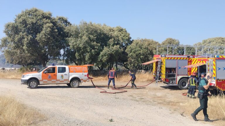 Un camión de bomberos rojo de la Comunidad de Madrid estacionado en una zona rural, con un bombero de pie cerca del vehículo, listo para la acción.