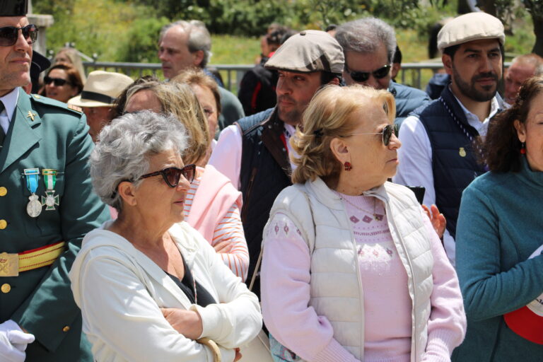 Un grupo diverso de personas, incluyendo mujeres mayores y hombres, observando atentamente la procesión de San Isidro en El Boalo bajo un sol brillante.