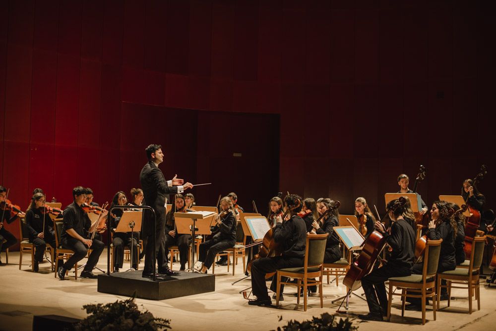 Una orquesta en un escenario, con un director de espaldas al público, frente a los músicos.