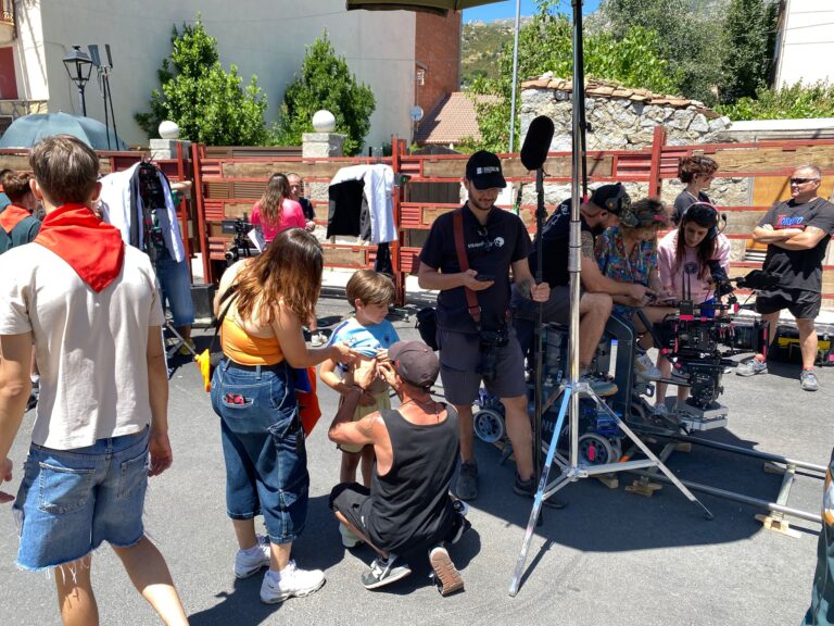 Equipo de rodaje de cine trabajando en una calle, con cámaras y micrófonos, mientras un niño pequeño interactúa con un adulto, mostrando el ambiente durante la filmación.