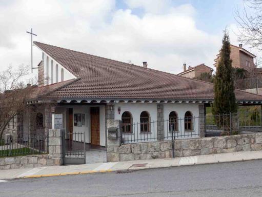 Iglesia de Santa Águeda con un diseño de tejado asimétrico y una cruz en la cúspide, muros blancos y de piedra, y una verja de metal.
