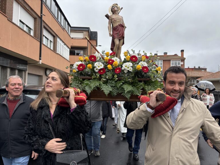 Varias personas, incluyendo hombres cargando una estatua adornada de San Sebastián, en procesión por una calle residencial en un día nublado, durante las Fiestas de San Sebastián en El Boalo, Cerceda y Mataelpino.