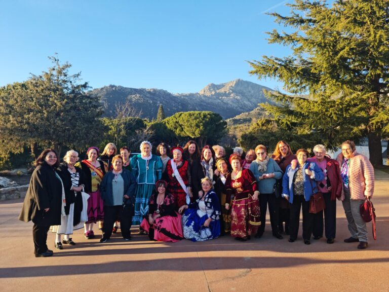 Un gran grupo de mujeres, varias de ellas con trajes tradicionales coloridos, posando al aire libre con montañas de fondo, durante las Fiestas de Santa Águeda en Mataelpino.