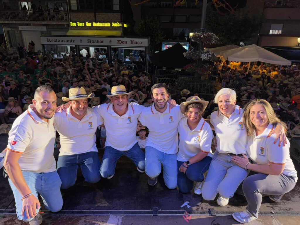 Grupo de siete personas, incluyendo al alcalde Sergio Yunquera y concejales de El Boalo, Cerceda y Mataelpino, posando en un escenario con sombreros de paja y camisetas blancas, con una multitud al fondo durante las Fiestas de El Boalo.