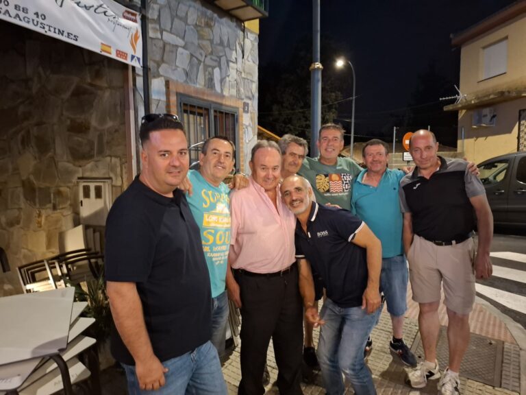 Grupo de ocho hombres, algunos con sombreros, sonriendo y posando en una calle iluminada por la noche, durante las Fiestas de El Boalo 2025.