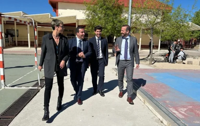 El Alcalde Sergio Yunquera y otros representantes caminan al aire libre, posiblemente en el exterior de un colegio, con el sol iluminando la escena.
