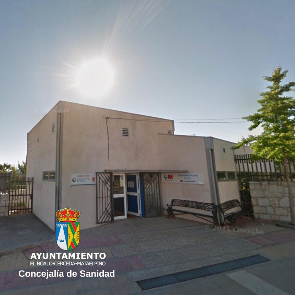 Fachada de un edificio de color beige bajo la luz del sol, con un banco de parque enfrente y un cartel de "Ayuntamiento El Boalo - Cerceda - Mataelpino Concejalía de Sanidad".