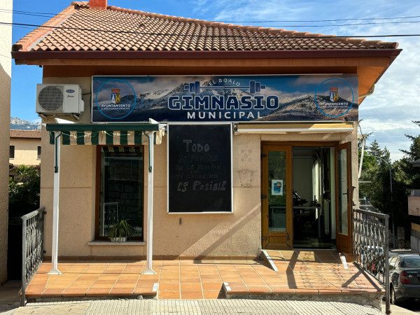 Fachada de un edificio beige con techo de tejas, un letrero que dice "GIMNASIO MUNICIPAL" y el logo del Ayuntamiento de El Boalo.