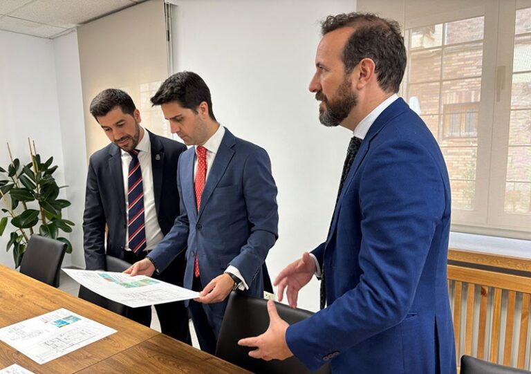 Tres hombres, incluido el Alcalde Sergio Yunquera, en trajes de negocios discutiendo documentos en una mesa de reuniones.