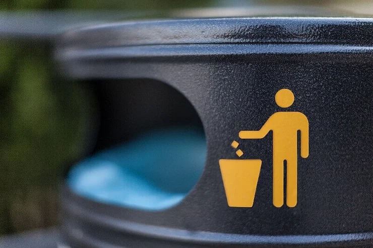 Un primer plano de un símbolo amarillo de una persona depositando basura en una papelera, sobre una superficie oscura y texturizada.