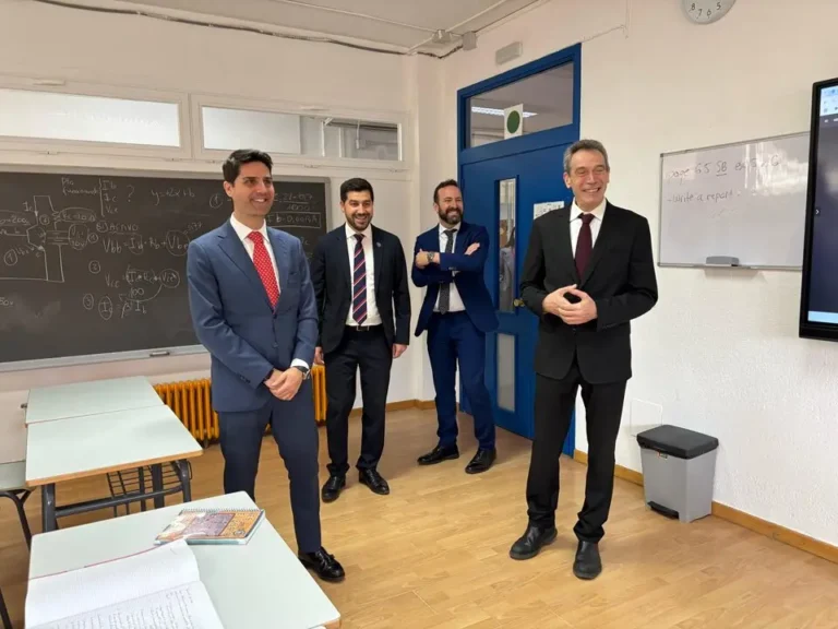 Cuatro hombres, incluido el alcalde Sergio Yunquera, de pie frente a una pizarra interactiva en un aula, con estudiantes sentados de espaldas.