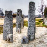 Grupo de monolitos de granito gris, parte de un antiguo potro de herrar, en un sendero de piedra bajo un cielo nublado.