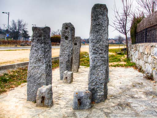 Grupo de monolitos de granito gris, parte de un antiguo potro de herrar, en un sendero de piedra bajo un cielo nublado.