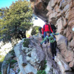 Grupo de excursionistas subiendo por un sendero rocoso junto a un acantilado de granito.
