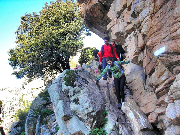 Grupo de excursionistas subiendo por un sendero rocoso junto a un acantilado de granito.