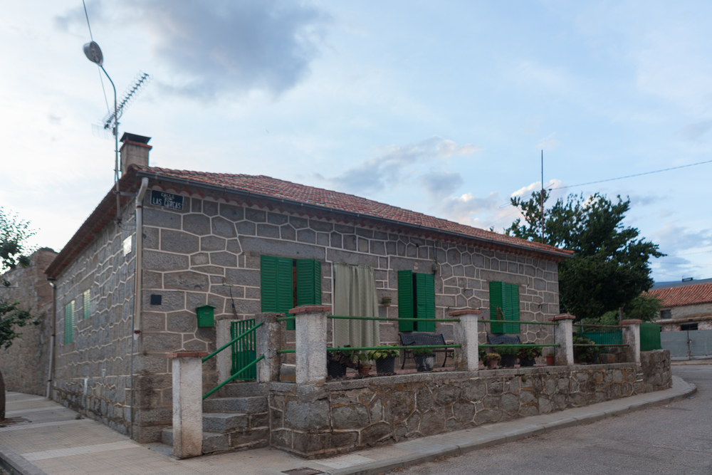 Una vivienda tradicional de piedra con tejado de tejas, contraventanas de madera verdes y un pequeño porche en la entrada.