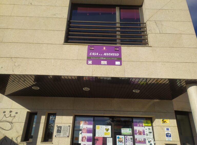 Fachada moderna de un edificio con revestimiento de piedra clara y grandes ventanales, y un cartel morado de "CASA de la JUVENTUD".